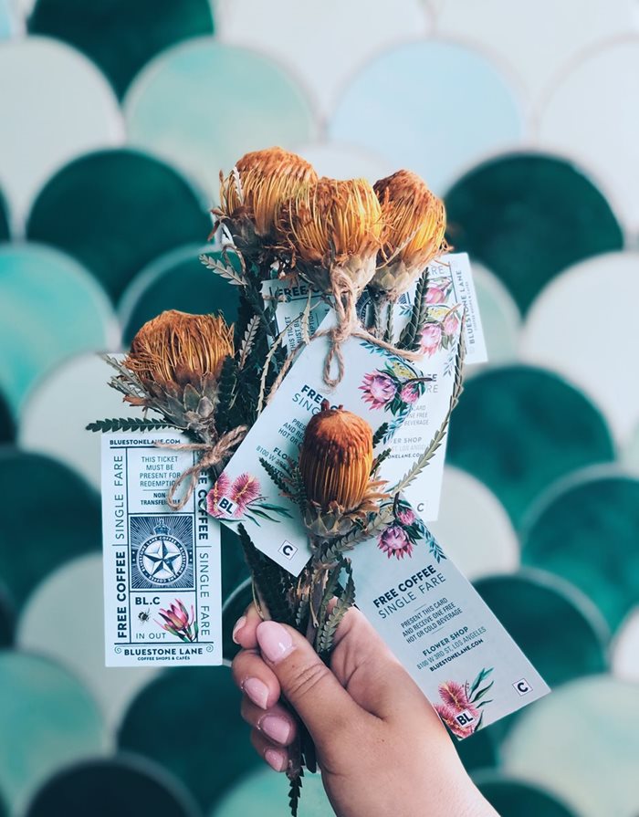 A woman's hand holding dried flowers with an advertisement for Bluestone Lane cafe.